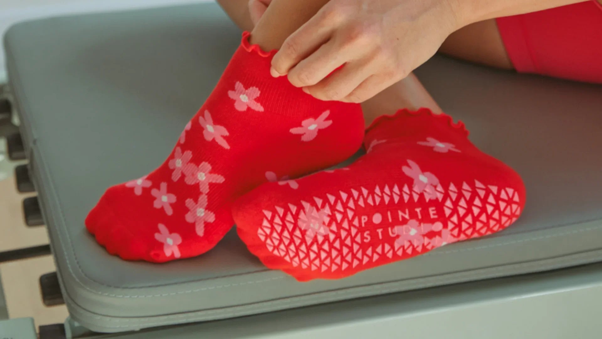Nærbillede af fødder iført røde Pointe Studio sokker med blomsterprint. Ideelle til at bringe lidt farve og glæde til din daglige rutine.